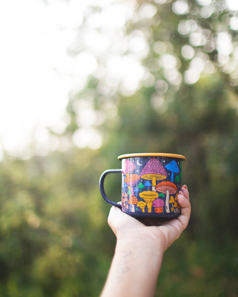Midnight Mushroom Enamel Mug 16oz held outdoors with colorful mushroom design in the sunlight