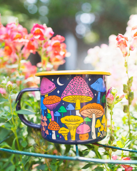 Midnight Mushroom Enamel Mug 16oz in a vibrant floral garden setting