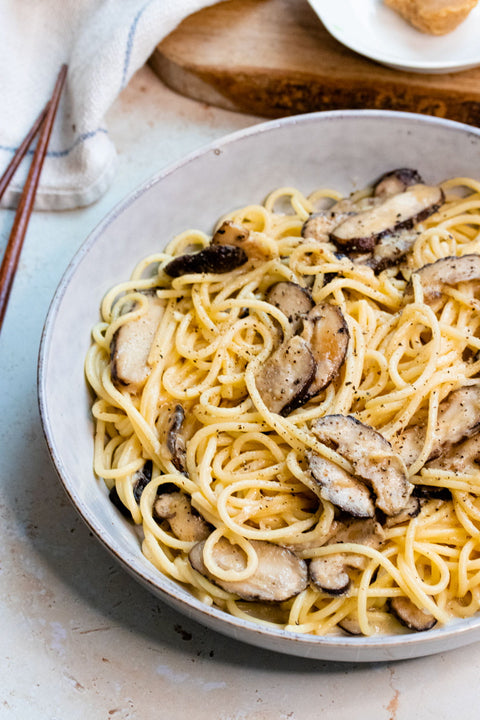 Pasta dish with creamy sauce and sliced mushrooms served in a white bowl on a rustic table setting.