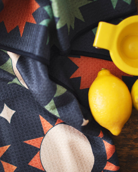 Moon Phase Kitchen & Tea Towel with vibrant moon and sun design next to lemons and a yellow juicer.