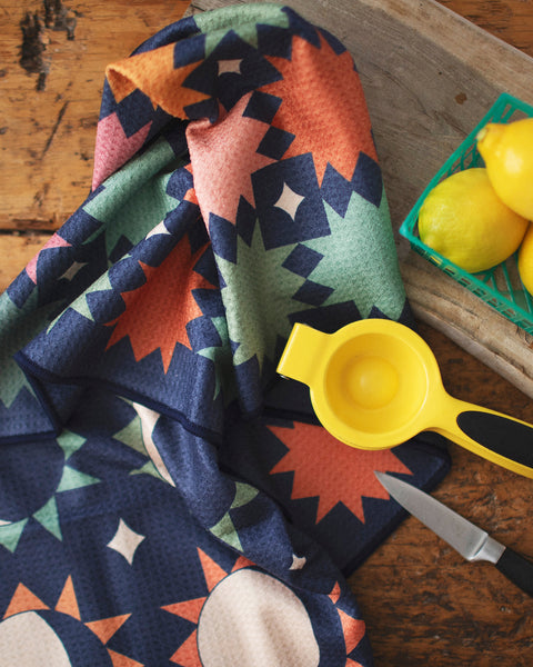 Moon Phase Kitchen & Tea Towel displayed with lemons and a juicer on a wooden table.
