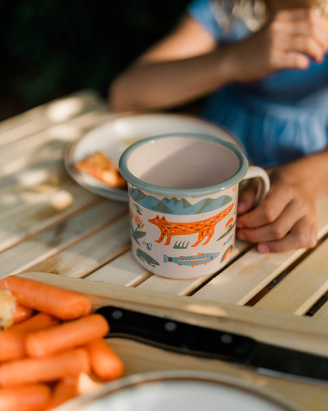 Mountain Stream Enamel Mug 16oz on a wooden table with food, perfect for cozy mornings.