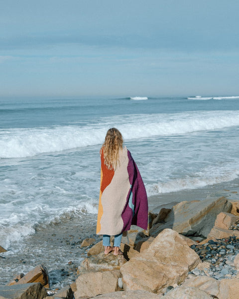 Cozy handwoven Mountain Sunrise Blanket made from recycled materials, perfect for versatility and warmth, by the ocean. By Trek Light.