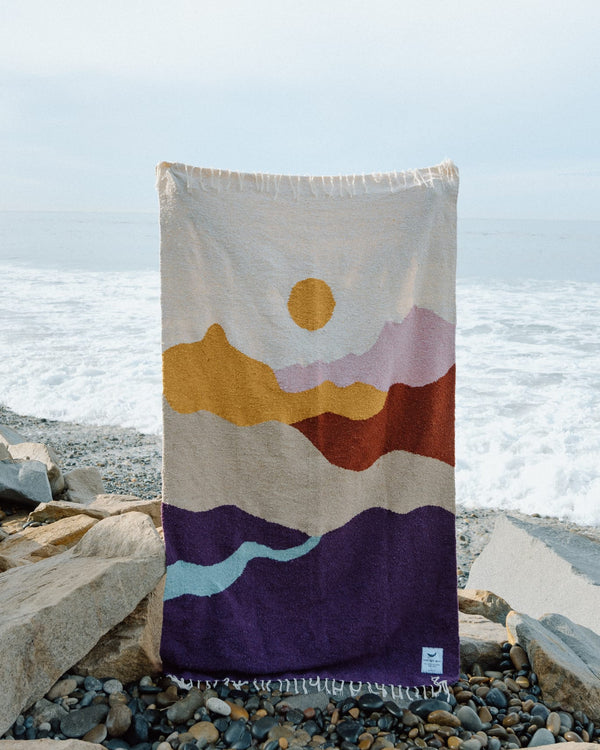 Cozy handwoven Mountain Sunrise blanket made from recycled clothing materials, showcasing beautiful and versatile design by the sea. By Trek Light.