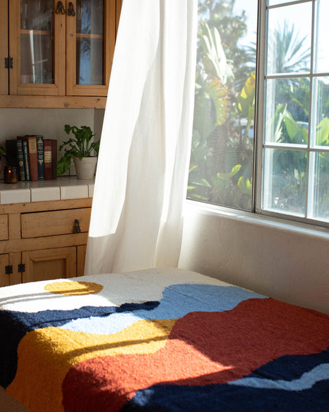 Vibrant handwoven Mountain blanket by Trek Light, capturing sunlight by a window, inviting warmth and artistic flair into your space.