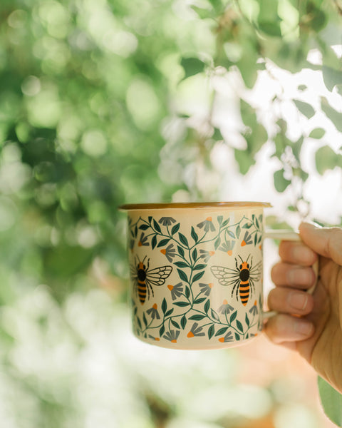 Honey Bee Enamel Mug 16oz with floral design held in hand, perfect for cozy mornings and outdoor adventures.