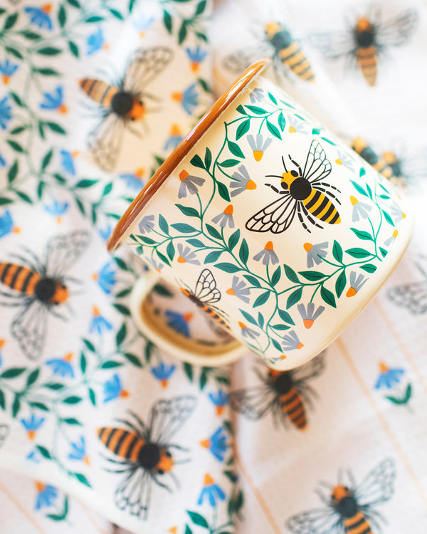 Honey Bee Enamel Mug 16oz with floral design and bees on a tablecloth, perfect for cozy mornings.