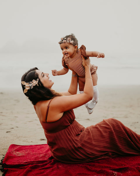 Woman lifting child joyfully on a Napa Blanket on the beach, enjoying a cozy moment together.