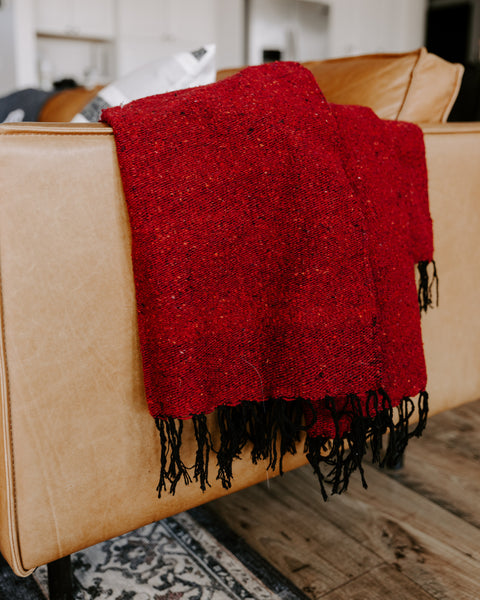 Napa Blanket draped over a chair, showcasing its rich red color and textured fabric for cozy living spaces.