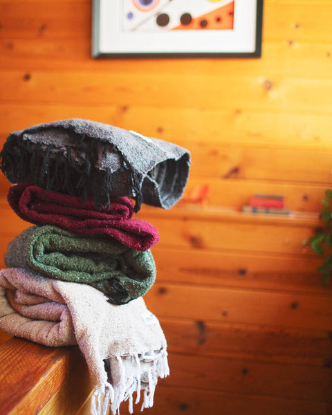 Stack of colorful Napa Blankets on a wooden surface, showcasing cozy textures and warm hues.