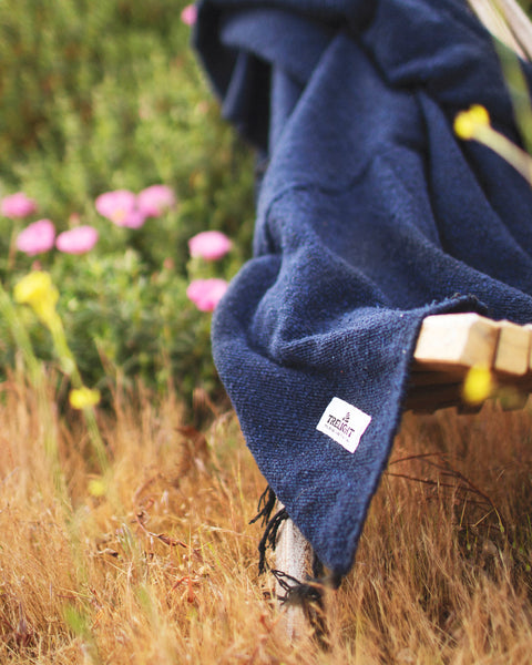 Newport Blanket draped over a bench, surrounded by flowers, emphasizing its coastal charm and eco-friendly design.