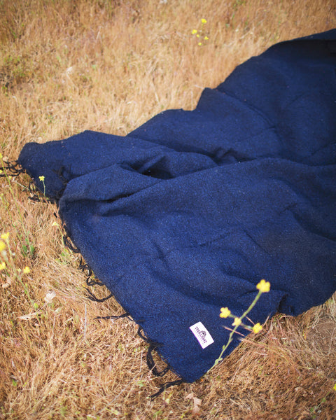 Newport Blanket laid out on dry grass, showcasing its rich color and texture, perfect for outdoor gatherings.