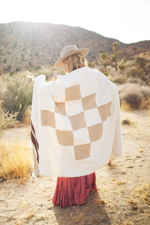 Cozy person wrapped in handwoven North Star blanket made from recycled materials, displaying beautiful natural tones and checker pattern. By Trek Light.