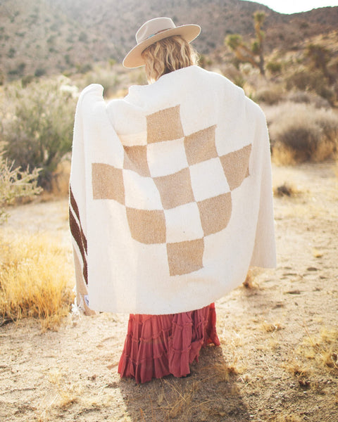 Cozy person wrapped in handwoven North Star blanket made from recycled materials, displaying beautiful natural tones and checker pattern. By Trek Light.