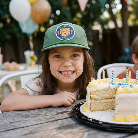 Child wearing a Party Animal Kids Hat, smiling with cake on face, celebrating a birthday party.