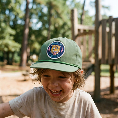 Child wearing Party Animal Kids Hat outdoors with playground in the background, smiling and enjoying a sunny day.