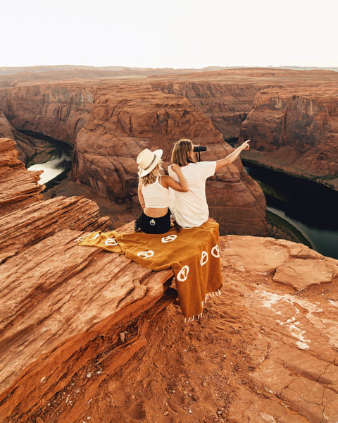 Two people enjoying nature wrapped in a Peace Blanket at a scenic canyon view, capturing a peaceful moment.