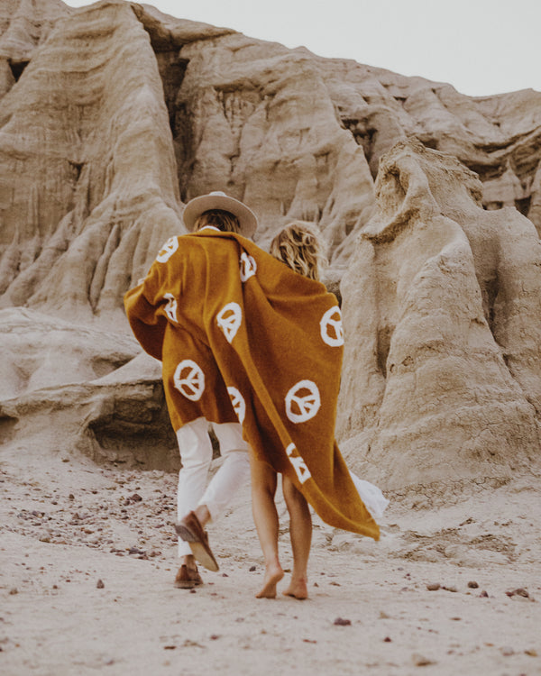 Couple wrapped in a Trek Light Peace Blanket made from 100% recycled clothing against a backdrop of scenic rock formations. Handwoven, cozy and beautiful.
