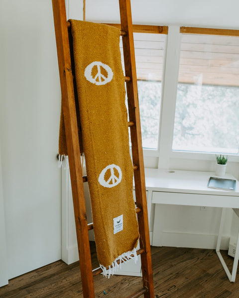 Cozy handwoven Peace Blanket from Trek Light on wooden ladder, made from recycled clothing materials.