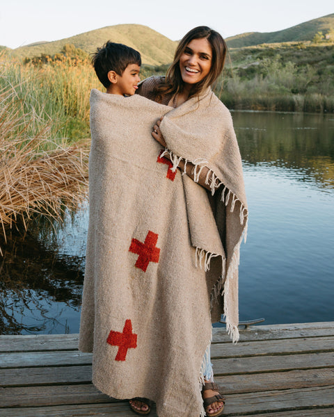 Mother and child wrapped in a Trek Light Positive Vibrations Blanket by the lake, featuring handmade recycled materials and unique design.