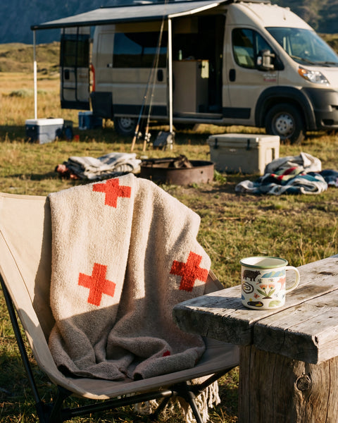 Positive Vibrations Blanket draped over a chair at a campsite with mountains and a van in the background.