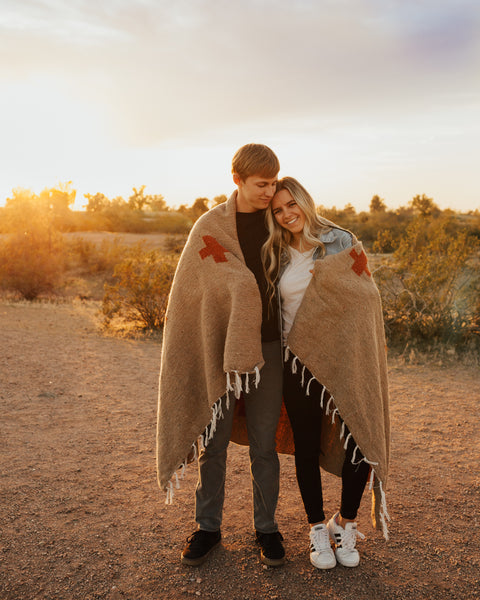 Couple embracing under the Positive Vibrations Blanket during sunset in a natural setting.