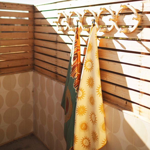 Sunny Wander & Travel Towel hanging on hooks in a stylish wooden setting, showcasing unique designs.
