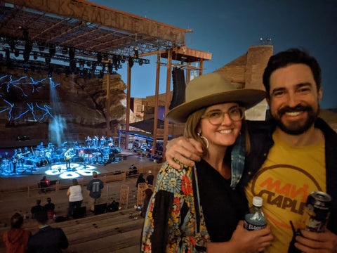 Couple smiling at an outdoor concert with stage lights at night