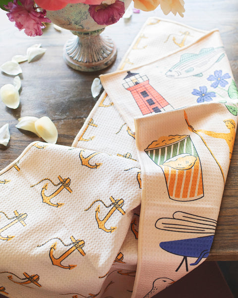 Rhode Island Kitchen & Tea Towel with vibrant anchor, lighthouse, and fish designs on a table.
