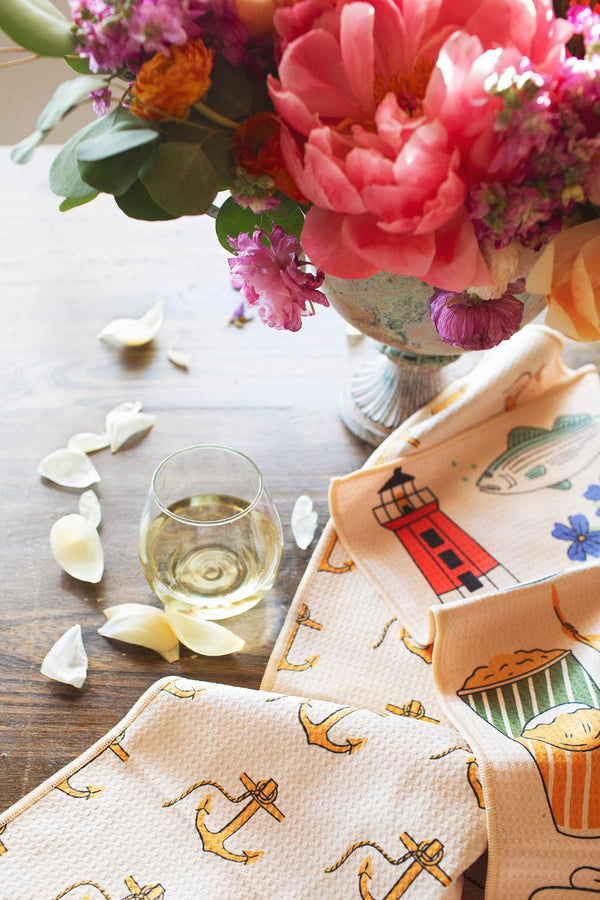 Rhode Island Kitchen & Tea Towel displayed with flowers and a glass of wine on a wooden table.