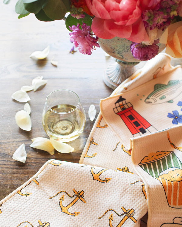 Rhode Island Kitchen & Tea Towel displayed with flowers and a glass of wine on a wooden table.