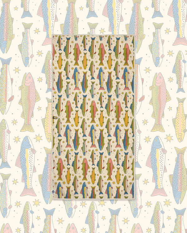 River Trout Wander & Travel Towel in cream with colorful trout and stars, laid over a matching fish pattern.