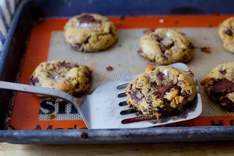 Freshly baked chocolate chip cookies on a baking tray with a spatula.