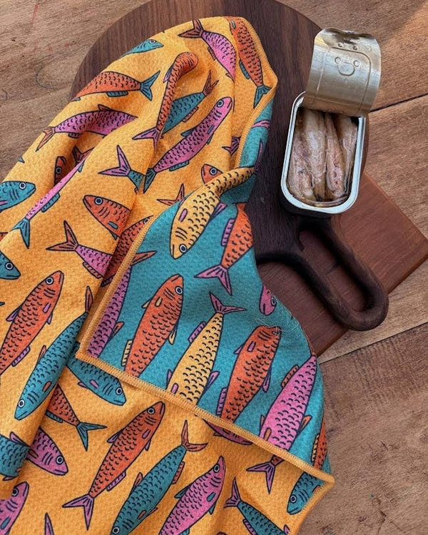 Sardine School Kitchen & Tea Towel on a wooden board with a tin of sardines, showcasing vibrant fish patterns.