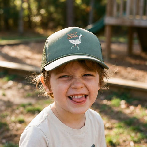 A child wearing a Silly Goose Kids Hat, smiling joyfully with a playful expression on a sunny day outdoors.