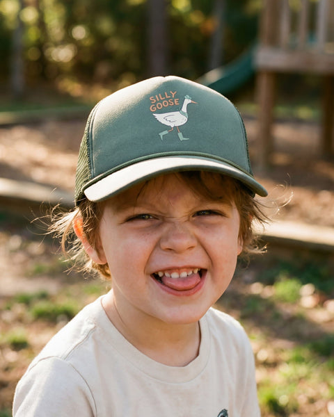 A child wearing a Silly Goose Kids Hat, smiling joyfully with a playful expression on a sunny day outdoors.