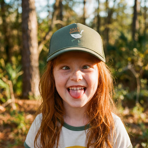 Child wearing a Silly Goose Kids Hat, smiling outdoors in a natural setting.
