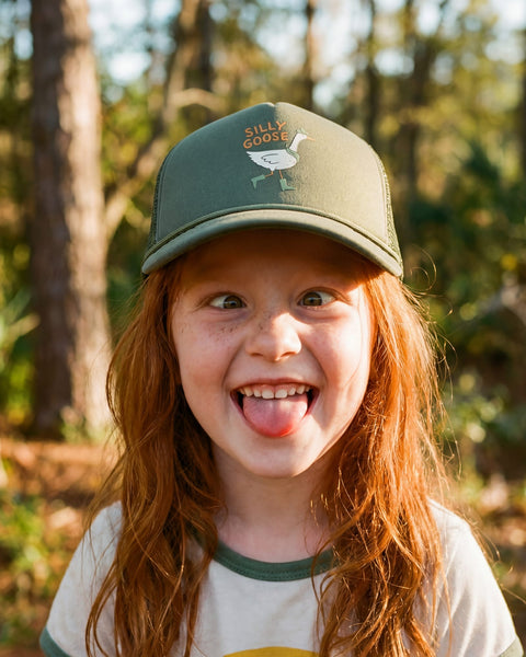 Child wearing a Silly Goose Kids Hat, smiling outdoors in a natural setting.