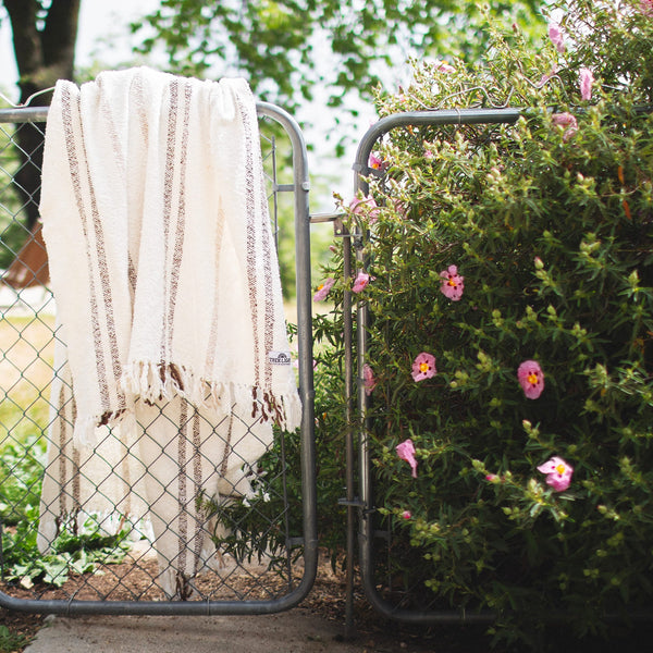 Silverton Blanket with geometric stripe pattern hanging on a garden gate, made from recycled materials and handwoven for unique style.
