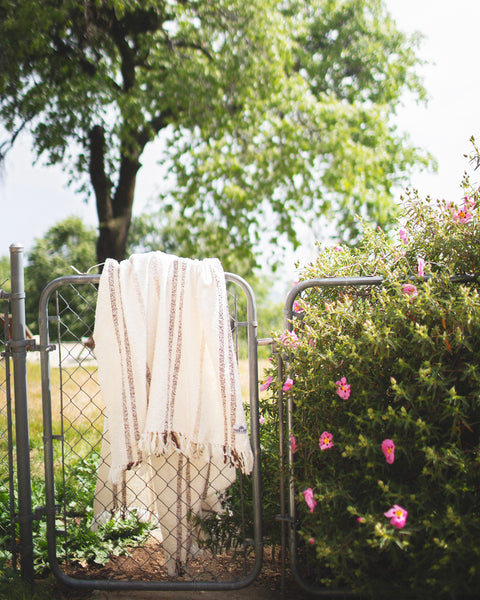 Silverton Blanket hanging on a gate surrounded by greenery and flowers, ideal for outdoor use.