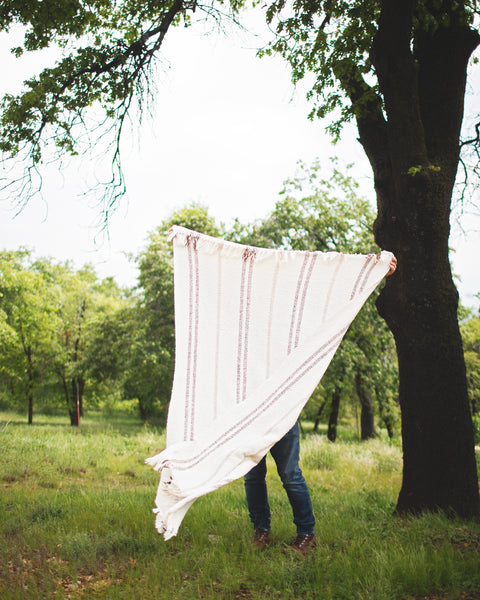 Person holding a Silverton Blanket outdoors under a tree, showcasing its lightweight design and stylish stripes.