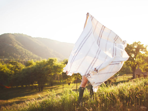 Person holding the Silverton Blanket with geometric stripes outdoors, highlighting its sustainable, handwoven design from recycled materials.