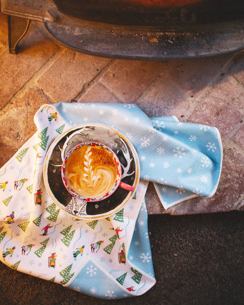 Cozy scene featuring a Snow Day Kitchen & Tea Towel with a steaming cup of coffee by the fireplace.