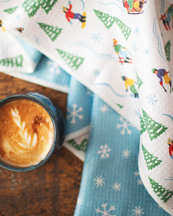 Snow Day Kitchen & Tea Towel with vibrant winter design, eco-friendly, super absorbent Grip-Texβ’ fabric, displayed with a cup of coffee.