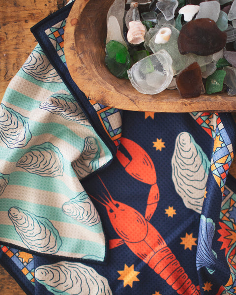 Snug Harbor Kitchen & Tea Towel featuring lobsters, oysters, and nautical patterns on a wooden surface.