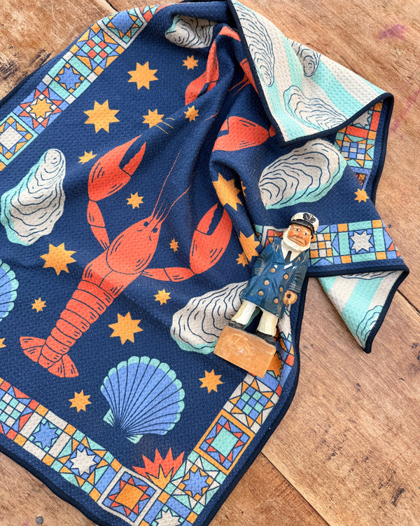 Snug Harbor Kitchen & Tea Towel featuring lobsters and nautical designs on a textured background.