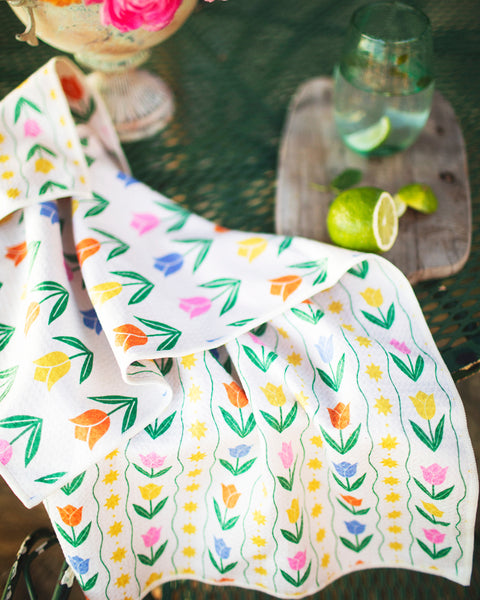 Spring Tulips Kitchen & Tea Towel with colorful tulip design on a table with flowers and a refreshing drink.