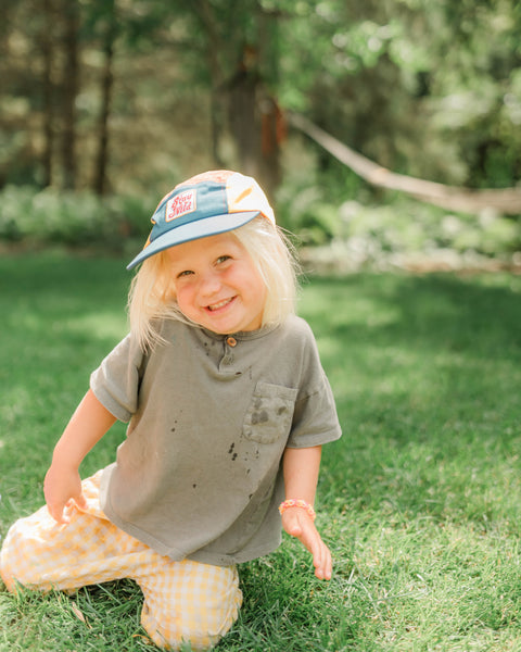 Child wearing a Stay Wild Kids Hat outdoors, smiling and playing in the grass, perfect for everyday adventures.