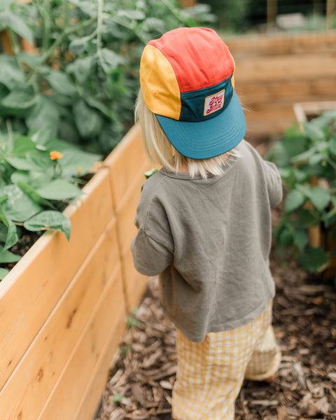 Child wearing a colorful Stay Wild Kids Hat while exploring a garden.
