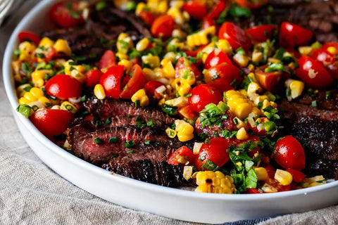 Grilled steak salad with cherry tomatoes, corn, and fresh herbs served in a white platter.